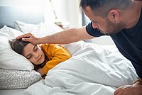 Ein krankes Kind in einem Bett wird von einem Erwachsenen getröstet